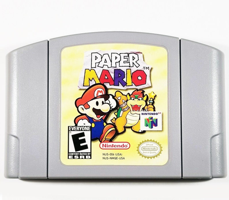 May include: A Nintendo 64 game cartridge for Paper Mario. The cartridge is yellow with a picture of Mario, Bowser, and a star on the front. The game is rated E for Everyone by the ESRB.