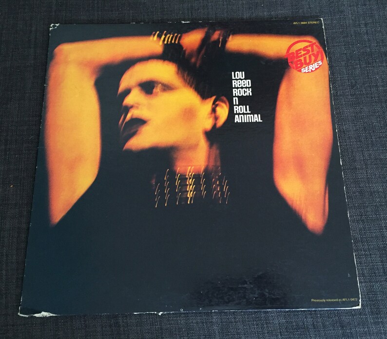 May include: A vinyl record cover featuring a close-up of Lou Reed's face. The cover is yellow and orange with the text "Lou Reed Rock 'n' Roll Animal" and "Best Buy Series" in white.
