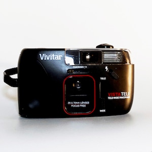 May include: A black Vivitar Vista Tele camera with a red and white label that reads "35 & 70mm LENSES FOCUS FREE" and "VISTA TELE TELE-WIDE PANORAMA".