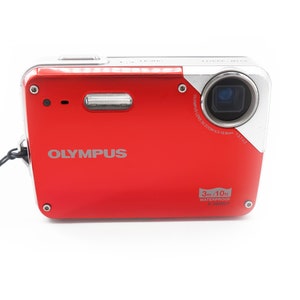 May include: A red Olympus digital camera with a silver lens and a black strap. The camera is waterproof up to 10 feet (3 meters).