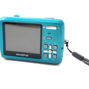 May include: A teal blue digital camera with a black strap. The camera has a silver button panel with the word "OLYMPUS" printed on the front.