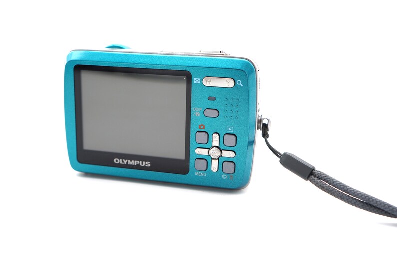 May include: A teal blue digital camera with a black strap. The camera has a silver button panel with the word "OLYMPUS" printed on the front.