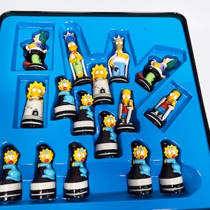 May include: A blue and yellow Simpsons chess set with all the pieces in place on a blue board. The pieces are made of plastic and feature the characters from the Simpsons television show.