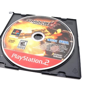 May include: A PlayStation 2 DVD game disc titled "Shadow the Hedgehog" in a black case. The disc features a character illustration and the PlayStation 2 logo. The game is rated "E10+" for Everyone 10 and up.