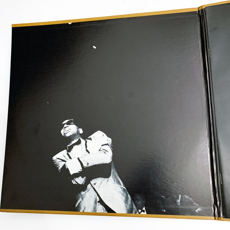 Pu&ograve; includere: Fotografia in bianco e nero di un uomo in giacca e cravatta, che guarda in alto. L'immagine &egrave; su uno sfondo nero con un bordo dorato. L'uomo &egrave; nella parte inferiore dell'immagine, con la maggior parte dell'immagine che &egrave; lo sfondo nero.