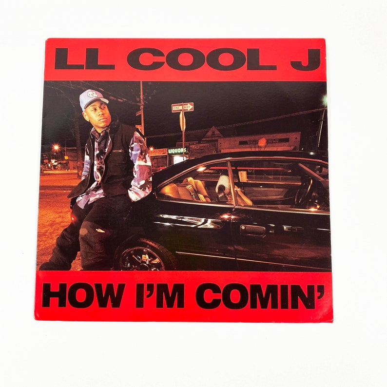 May include: A red album cover with the text "LL COOL J" in large white letters and "HOW I'M COMIN'" in smaller white letters. The cover features a photo of a man in a blue hat and a black vest leaning against a black car in a city street at night.