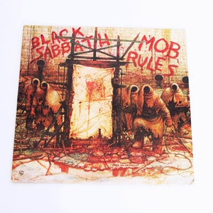 May include: A vintage vinyl record album cover featuring a red and black graphic design with the text "Black Sabbath Mob Rules". The cover art depicts three hooded figures in a dark, urban setting.