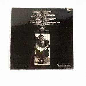 May include: Black and white photo of a man wearing a hat and suit, sitting on a set of stairs. The back of a vinyl record album with a list of songs on each side. The album is titled "Come Fly With Me" by Frank Sinatra.