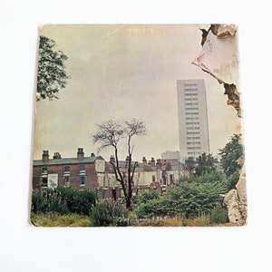 May include: A vintage record album cover featuring a faded, sepia-toned image of a city street scene. The album cover has a torn edge and shows a tall building, brick houses, and trees.