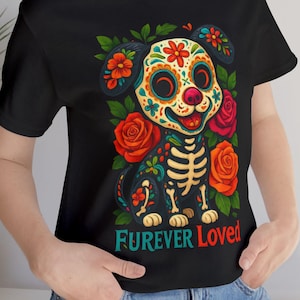 May include: Black t-shirt featuring a colorful cartoon dog with a sugar skull design, surrounded by red and orange roses. The text "Furever Loved" is printed in a script font at the bottom of the graphic.