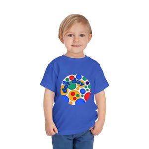 May include: A blue toddler t-shirt featuring a colorful circular design with the words "Fun Day" in green, blue, and yellow. The design includes various sized circles in red, yellow, and blue. The shirt is made of soft material.