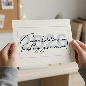 Może przedstawiać: Prostokątna biała kartka okolicznościowa z cienką szarą ramką i napisem "Congratulations on finishing your exams!" wykonanym czarną kursywą, z jasnoszarymi cyframi "2026" widocznymi w tle kartki.