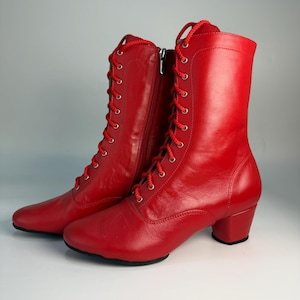 May include: A pair of vibrant red ankle boots featuring a lace-up closure and a side zip. The boots have a rounded toe and a small block heel. The laces and zip are also red. The boots are made of a smooth, leather-like material.
