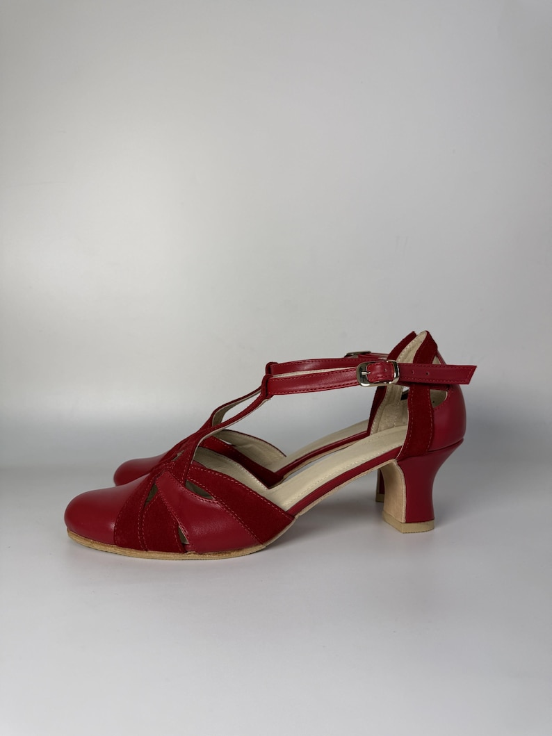 Puede incluir: Un par de zapatos rojos con correa en T que presentan una combinaci&oacute;n de texturas lisas y tipo ante. El calzado incluye una puntera redondeada, un tac&oacute;n de bloque de altura media y una correa de tobillo ajustable con una peque&ntilde;a hebilla de metal dorado.