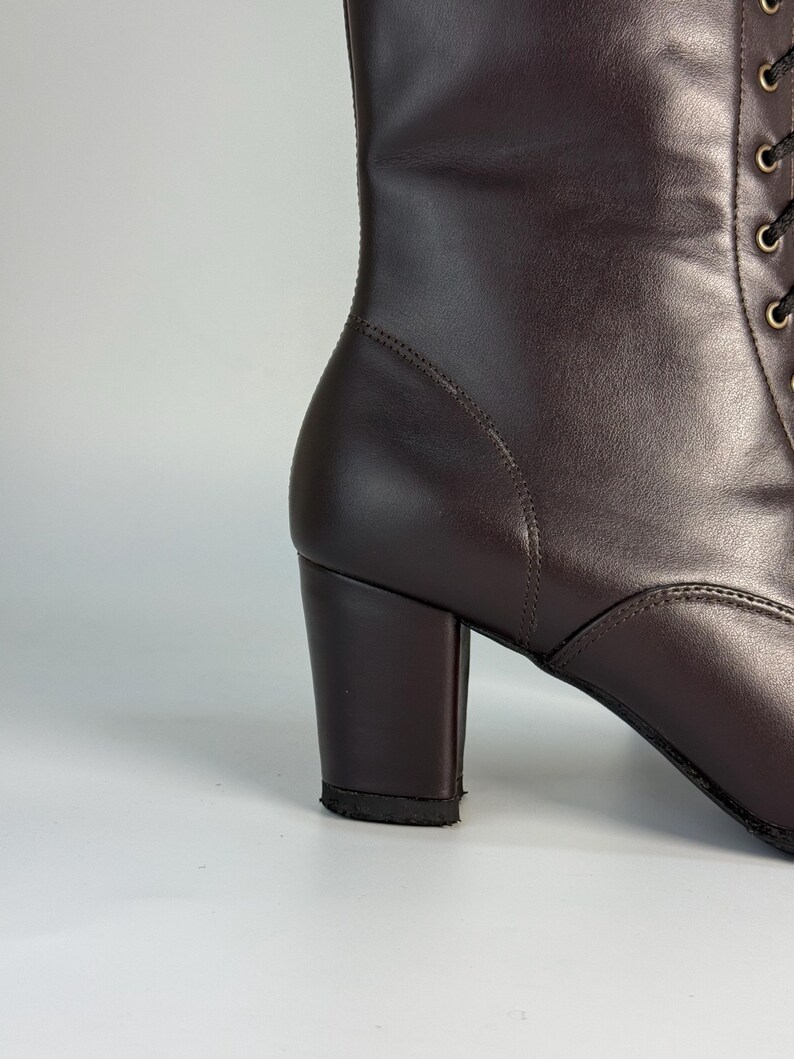 May include: A close-up of a dark brown leather boot with a block heel. The boot has a lace-up design and a rounded toe. The heel measures approximately 3 inches.