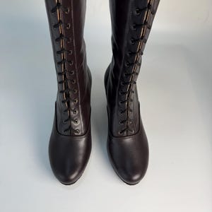 May include: A pair of dark brown knee-high boots with a lace-up design. The boots have a rounded toe and a subtle heel. The laces are black, and the boots appear to be made of leather.