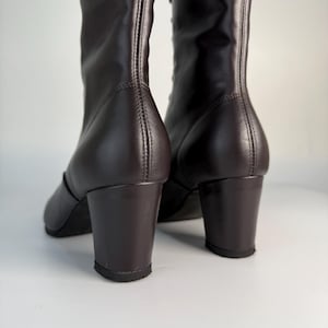 May include: A pair of dark brown leather boots with a block heel. The boots have a tall shaft and are laced up the front. The heels are approximately 2 inches high.