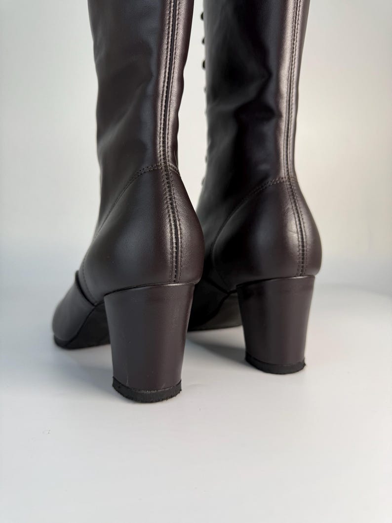 May include: A pair of dark brown leather boots with a block heel. The boots have a tall shaft and are laced up the front. The heels are approximately 2 inches high.