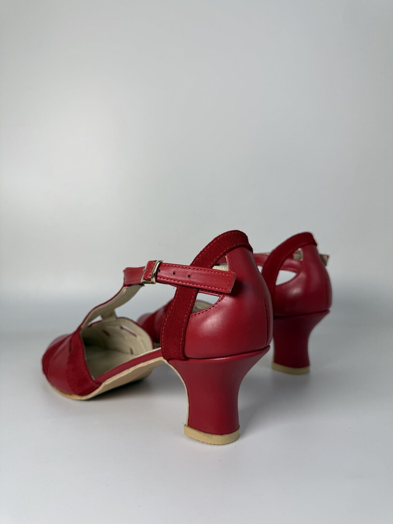 Puede incluir: Un par de zapatos de pulsera en T rojos con acabado en piel lisa y detalles en ante. Los zapatos tienen puntera redondeada, tac&oacute;n de bloque de altura media y una correa ajustable en el tobillo con una peque&ntilde;a hebilla de metal dorado.