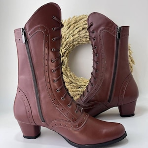 May include: A pair of mid-calf boots in a deep maroon color featuring a lace-up front with matching laces, side zippers, and decorative perforated detailing along the seams. The boots have a rounded toe and a low, block-style heel.