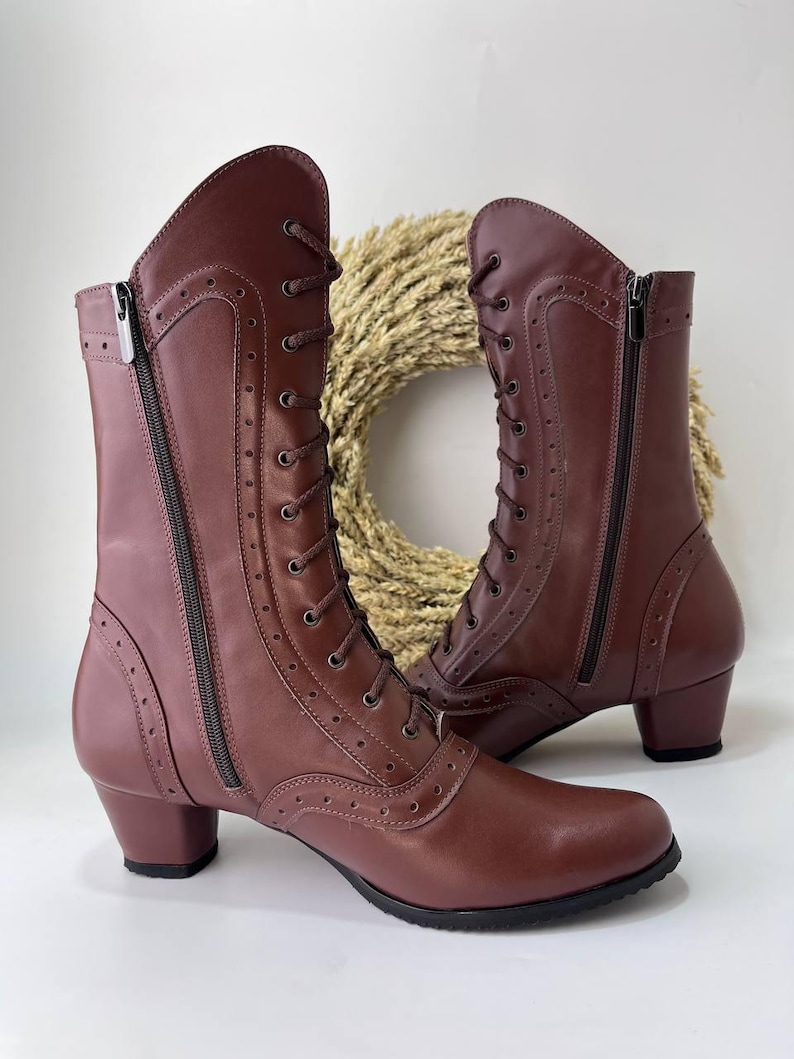 May include: A pair of mid-calf boots in a deep maroon color featuring a lace-up front with matching laces, side zippers, and decorative perforated detailing along the seams. The boots have a rounded toe and a low, block-style heel.