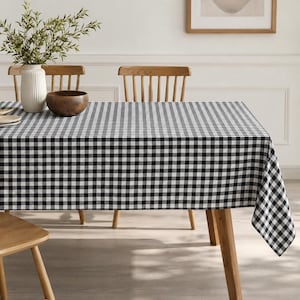 May include: A black and white checkered tablecloth covers a wooden table. A wooden bowl and a white vase with greenery sit on the table. Two wooden chairs are visible in the background.