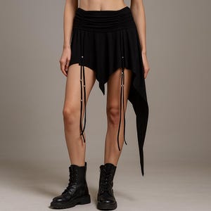 May include: Black asymmetrical skirt with a draped design. The skirt has a ruched waistband and decorative ties with metal accents. The skirt is worn with black combat boots.