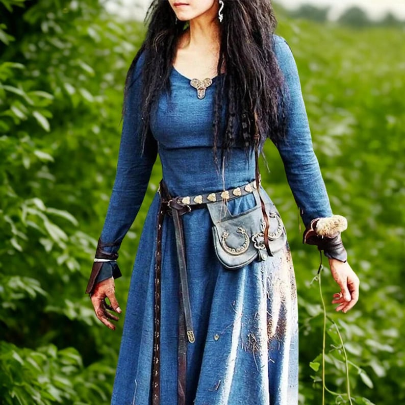May include: A long-sleeved, blue dress with a V-neck and a flowing skirt. The dress is accessorized with a brown leather belt, a small pouch, and wrist cuffs. The dress has a medieval or fantasy theme.