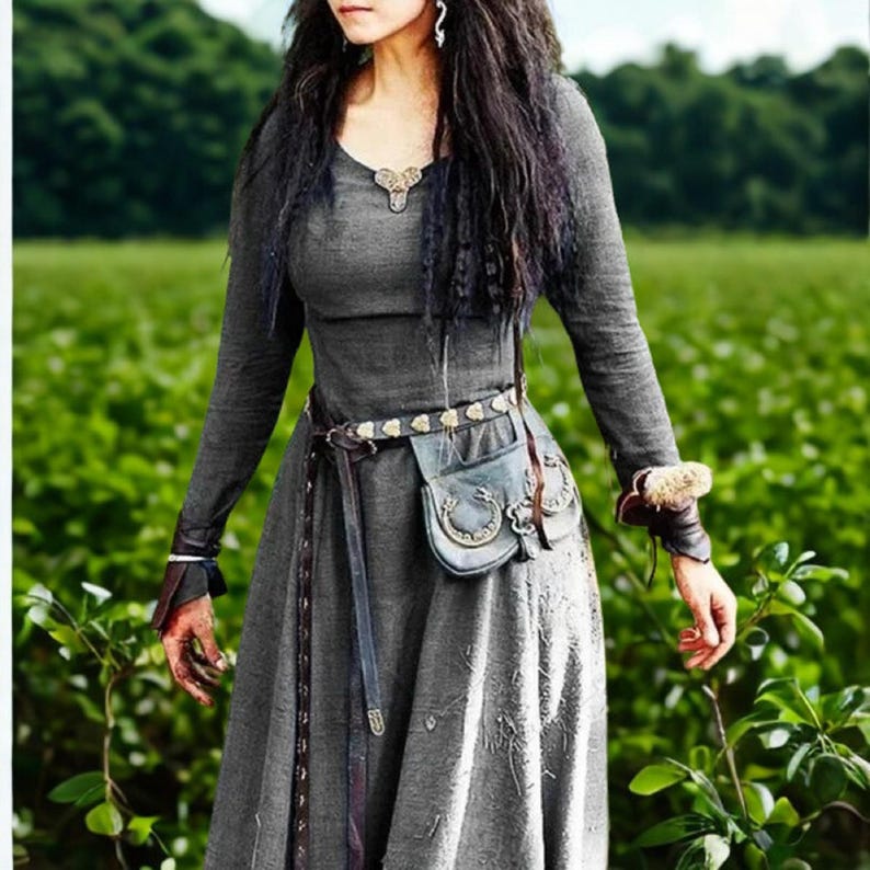May include: A long-sleeved gray dress with a decorative belt and a small pouch. The dress features a scoop neckline and is accessorized with a leather belt and wrist cuffs. The background is a green field.