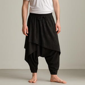 Puede incluir: Pantalones harén negros con una superposición asimétrica. Los pantalones tienen una cintura con cordón y están hechos de una tela suave y fluida. El diseño presenta un efecto de capas único, que ofrece un aspecto moderno y elegante.