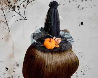 Puede incluir: Un accesorio para el cabello en forma de mini sombrero de bruja negro con una corona de tul puntiaguda y un ala con volantes. El sombrero está decorado con una pequeña calabaza naranja, una silueta de murciélago negro brillante y una escoba.
