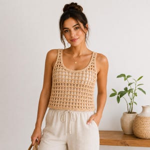 Può includere: Una canotta in crochet beige caratterizzata da un motivo a rete aperto, scollo rotondo e spalline larghe. Il capo è senza maniche, presenta un orlo dritto ed è realizzato in filato di colore chiaro con una trama visibilmente intrecciata.