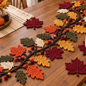 May include: A crochet table runner featuring a long dark brown vine adorned with various autumn-colored leaves in shades of red, orange, yellow, olive green, and cream, interspersed with small round berries, accompanied by matching leaf coasters.
