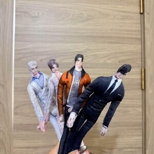 May include: Four fabric dolls dressed in different outfits. One doll wears a black suit with a white tie, another a jacket with an orange exterior, and the others wear light-coloured suits. The dolls have painted faces and are held together.