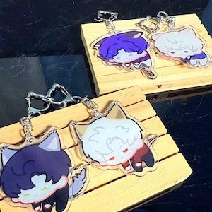 May include: Four clear acrylic keychains featuring cartoon cat characters with different colored hair and outfits. Each keychain has a silver metal clasp. The keychains are displayed on small wooden pallets.
