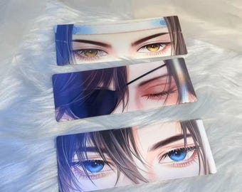 Könnte beinhalten: Drei rechteckige Lesezeichen mit detaillierten Illustrationen von Augen im Anime-Stil. Die Augen sind in verschiedenen Farben, darunter Braun, Rot und Blau, mit dunklen Haaren und Hauttönen. Die Lesezeichen sind vor einem weißen, flauschigen Hintergrund platziert.