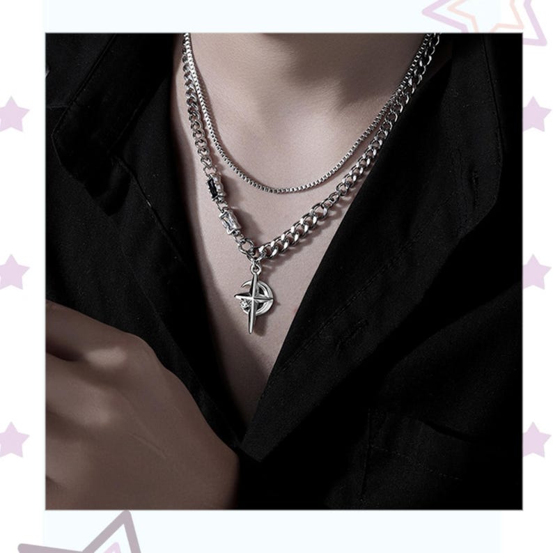 May include: A silver-toned necklace set featuring a curb chain and a thinner box chain. The pendant is a compass design. The necklace is worn against a black shirt.