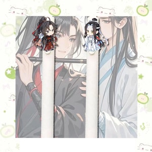 Peut inclure: Deux figurines de personnages de style anime, l'une en rouge et noir, l'autre en blanc et bleu, sont positionnées sur des objets cylindriques blancs. L'arrière-plan présente une illustration floue de deux personnages d'anime. L'image a une bordure décorative avec des éléments de dessins animés.