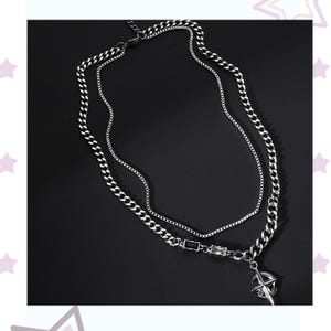 May include: A silver-toned layered necklace with a compass pendant. The necklace features two chains: a thicker curb chain and a thinner cable chain. The compass pendant is detailed with directional markings. The necklace is displayed against a dark background.