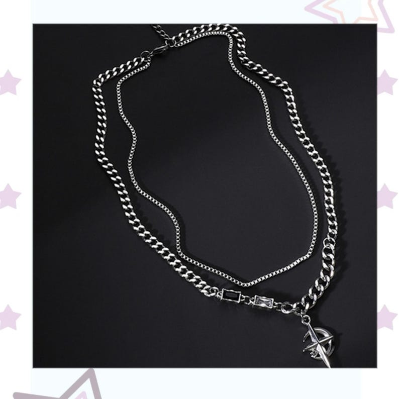 May include: A silver-toned layered necklace with a compass pendant. The necklace features two chains: a thicker curb chain and a thinner cable chain. The compass pendant is detailed with directional markings. The necklace is displayed against a dark background.