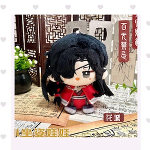 May include: A plush doll with black hair and a red outfit. The doll has a detailed face with embroidered features and is wearing a red coat. The doll is a collectible item.