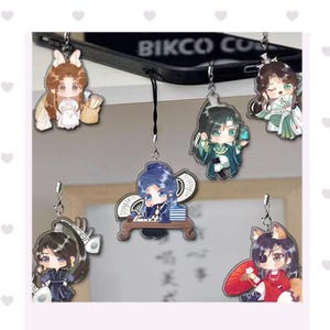 Puede incluir: Una colección de colgantes de personajes de estilo anime. Cada colgante presenta un personaje diferente con atuendos y accesorios únicos. Los colgantes están sujetos a una cadena plateada y cuelgan de un teléfono negro. El texto "BIKCO CO" es visible en el teléfono.