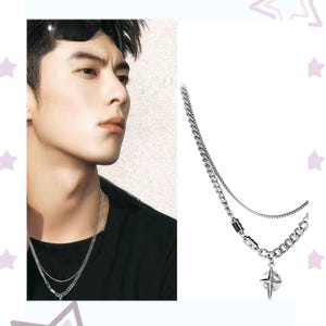 May include: A silver-toned necklace with two chains. The top chain is delicate, while the bottom chain is thicker and features a compass pendant. The necklace is shown on a person wearing a black shirt.