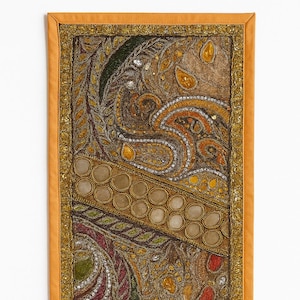 May include: Rectangular wall hanging with an intricate paisley design. The tapestry features a mix of gold, brown, and green hues, with reflective embellishments. The border is a solid orange color, with a gold trim.