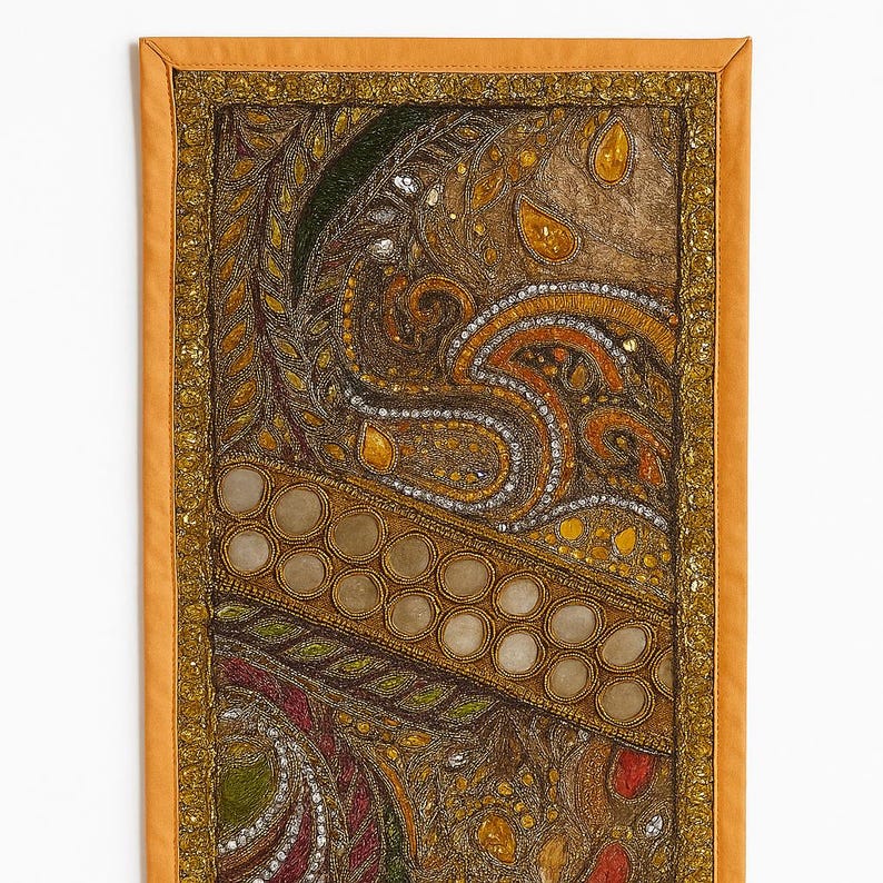 May include: Rectangular wall hanging with an intricate paisley design. The tapestry features a mix of gold, brown, and green hues, with reflective embellishments. The border is a solid orange color, with a gold trim.