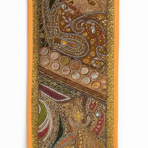 May include: A rectangular, ornate textile panel with a gold border. The panel features intricate embroidery in shades of brown, gold, green, and red. Circular and paisley patterns are visible, with embellishments of sequins and beads.