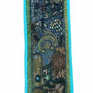 May include: A rectangular, ornate textile in shades of teal, navy, and gold. The design features floral and paisley patterns, embellished with sequins and beads. The edges are trimmed with a turquoise border and a green and gold patterned border.