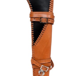 May include: A brown leather quiver with a black interior. The quiver has decorative stitching along the edges and is secured with two adjustable straps with metal buckles. A decorative silver-colored metal piece is on the bottom.