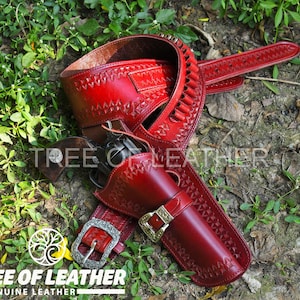 May include: A red leather gun belt and holster set with decorative stitching and a silver buckle. The set includes a belt with bullet loops and a holster for a revolver. The image also shows the text "TREE OF LEATHER GENUINE LEATHER".