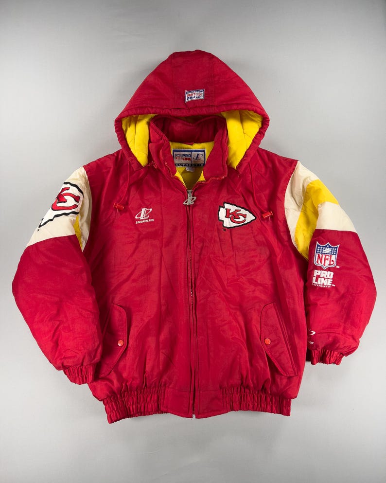 May include: Red hooded jacket with yellow lining and white and yellow accents. Features the Kansas City Chiefs logo on the chest and sleeve, with "NFL Pro Line" branding. A vintage, zip-up, winter coat.